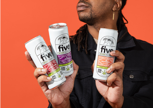 Man holding three Five THC Seltzer cans (Black Cherry, Guava Passionfruit, Grapefruit) against an orange background
