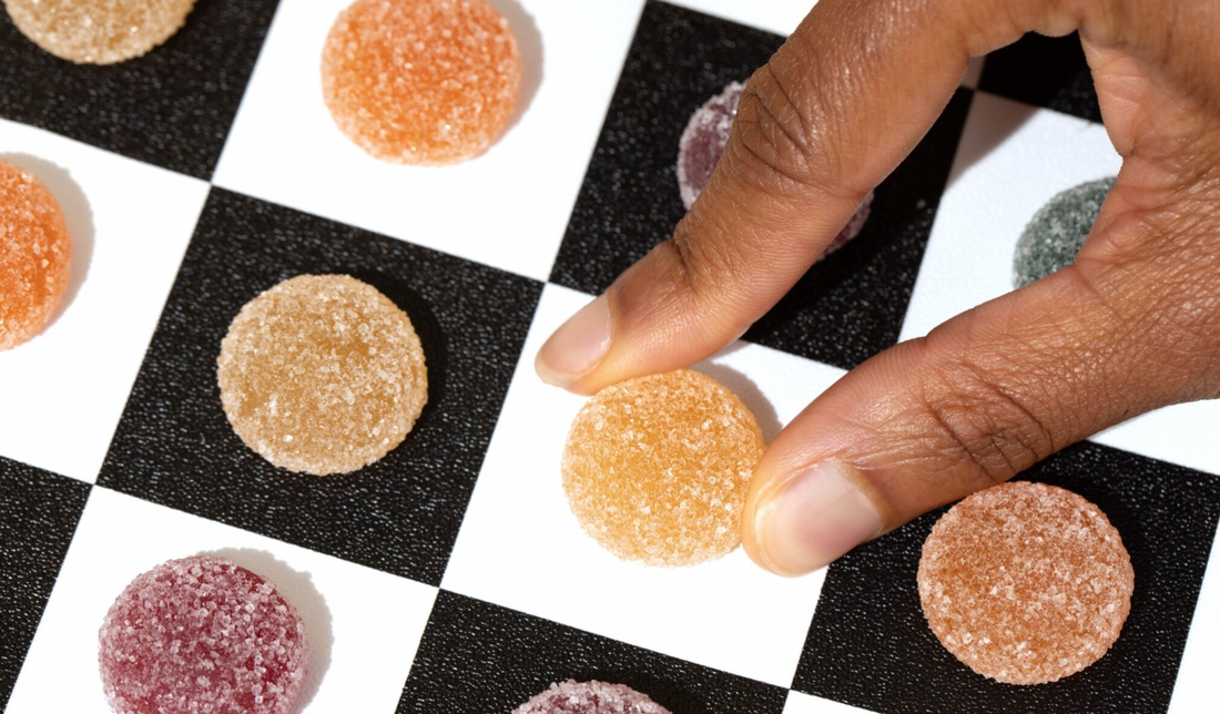 Close-up of sugar-coated round gummy being picked up by hand on a black-and-white checkerboard surface