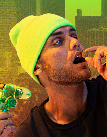 Person wearing a neon-green beanie holds a green vaporizer while bringing a small edible to their mouth.